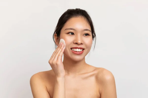 Genç Asyalı kadın yüzünü pamukla temizliyor. — Stok fotoğraf