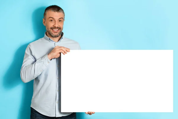 Hombre de mediana edad mostrando tablero de papel vacío sobre fondo azul — Foto de Stock