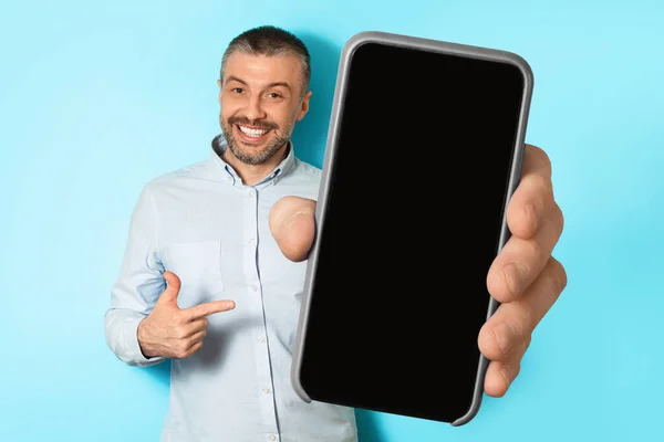 Uomo di mezza età che mostra lo schermo vuoto del telefono su sfondo blu — Foto Stock