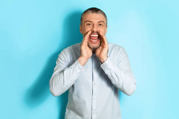 Middle Aged Man Shouting Holding Hands Near Mouth, Blue Background — Stockfoto