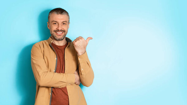 Man Pointing Thumb Finger Aside At Copy Space, Blue Background