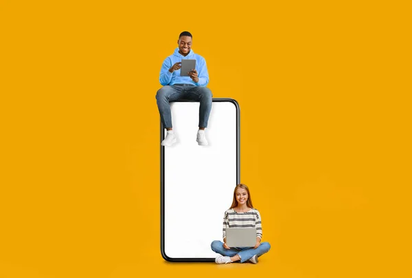 Couple sitting on white empty smartphone screen and using gadgets — Stok fotoğraf