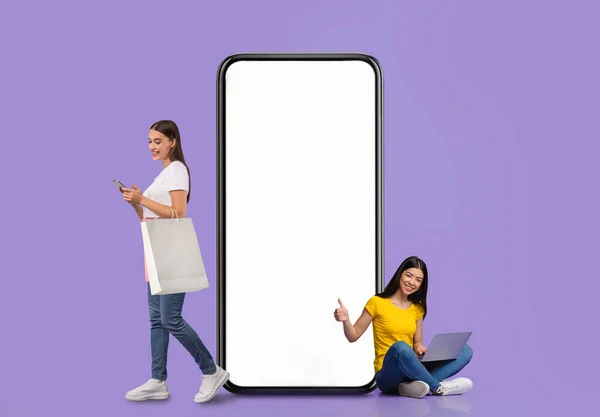 Women posing with white empty smartphone screen and shopper bags — Photo