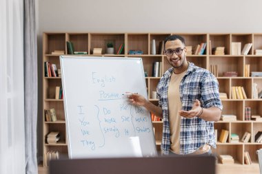 Online eğitim. Beyaz tahtayı işaret eden ve İngilizce dil bilgisi kurallarını açıklayan neşeli Arapça erkek öğretmenin portresi
