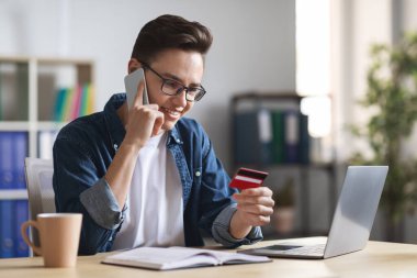 İnternetten alışveriş. Genç girişimci cep telefonuyla konuşuyor ve kredi kartı tutuyor.
