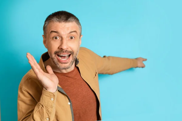 Middle Aged Man Pointing Finger Aside Advertising Offer, Blue Background — стокове фото