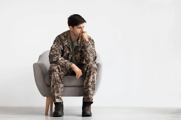 Pensive soldier sitting at armchair over white background — Stok fotoğraf