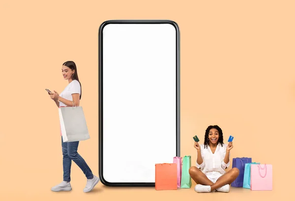 Women posing with white empty smartphone screen and shopper bags — Stok fotoğraf