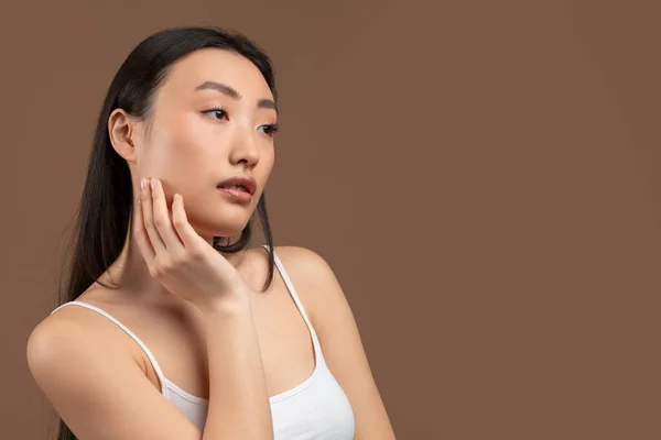 Spa facial concept. Beautiful asian lady touching her skin on cheek, enjoying result of beauty treatment, free space — Stockfoto