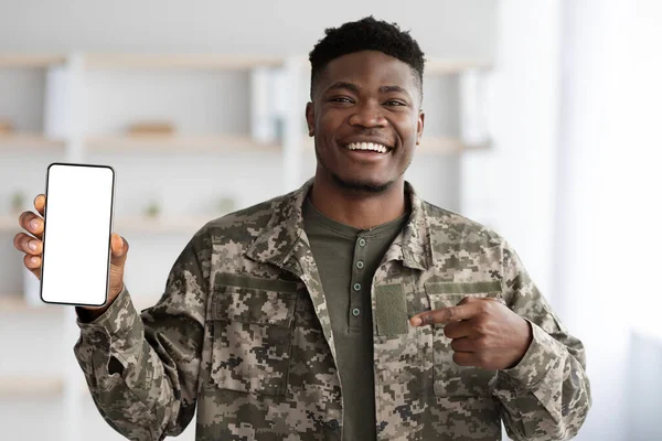 Šťastný černý voják ve vojenské uniformě ukazuje svůj smartphone, mockup — Stock fotografie