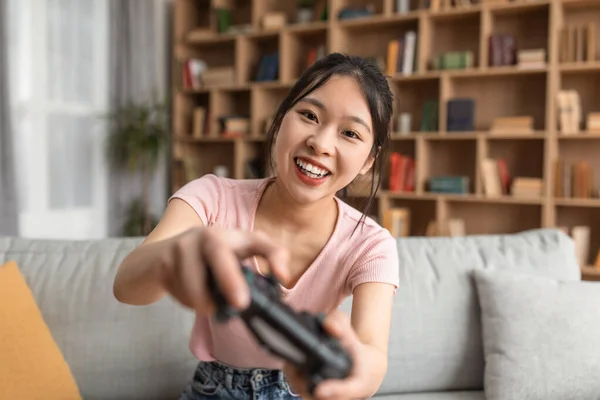 Playful korean lady using joystick and playing online video games, sitting on sofa in living room, closeup — Foto de Stock