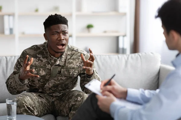 Duygusal askeri siyah adam psikoterapistle konuşurken el kol hareketi yapıyor.