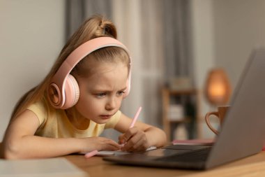 Dizüstü bilgisayar kullanan küçük kız evde ders alıyor.