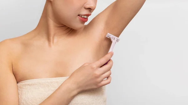 Closeup view of young Asian woman shaving armpit with razor — стокове фото