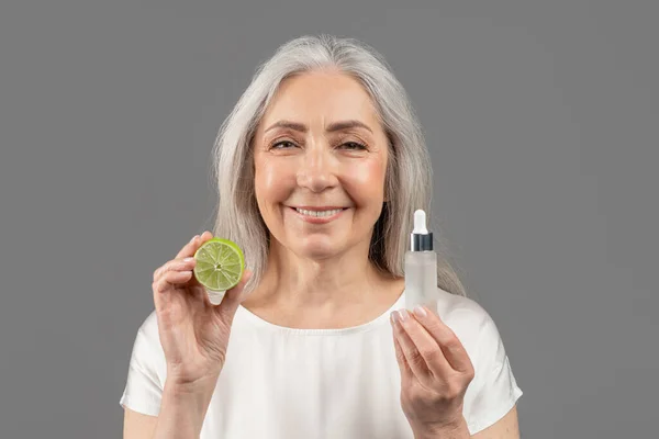 Daily skincare. Feminine mature woman advertising organic cosmetics, showing facial serum with fruit acids and lime — 스톡 사진