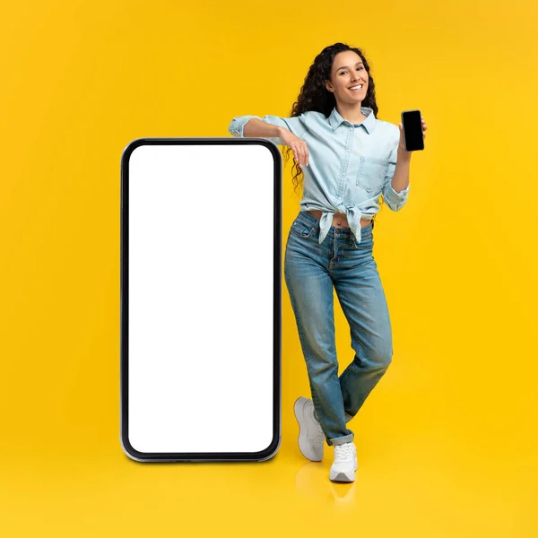 Donna che tiene lo schermo dello smartphone vuoto, appoggiata su un grande pannello — Foto Stock