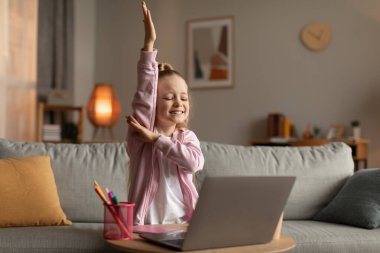 Dizüstü bilgisayar kullanan kız evde el kaldırıyor.