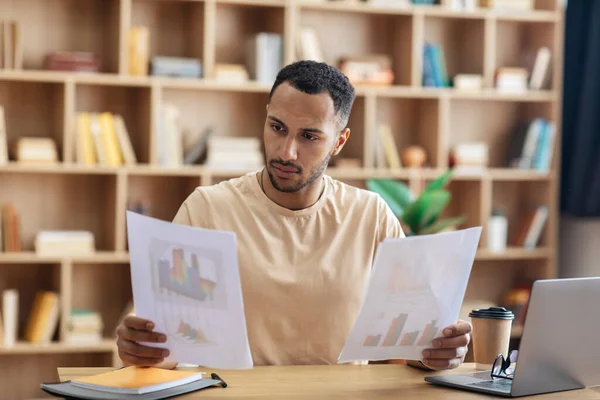 Focused arab man looking through documents, checking reports while having online meeting on laptop, sitting at home — Foto de Stock