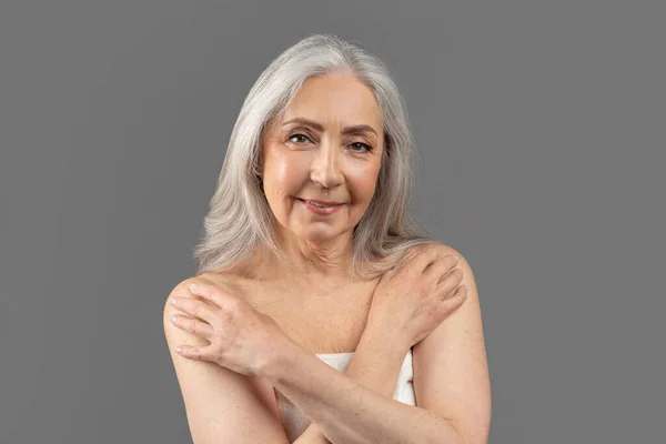 Beleza madura natural. Mulher idosa encantadora em toalha com pele lisa após o chuveiro, posando em fundo cinza — Fotografia de Stock