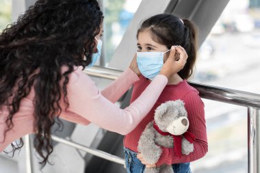 Anne, küçük kızına koruma maskesi takıyor. Havaalanında, yakın plan.