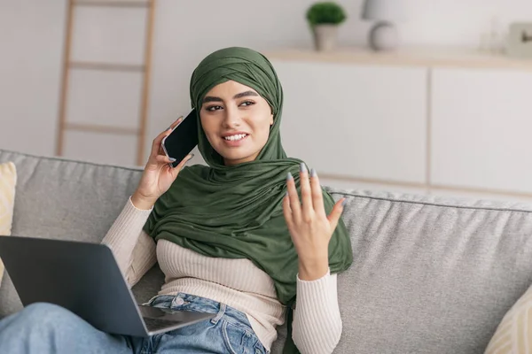 使用笔记本电脑、在家里用智能手机讲话、复制空间的阿拉伯积极女性 — 图库照片