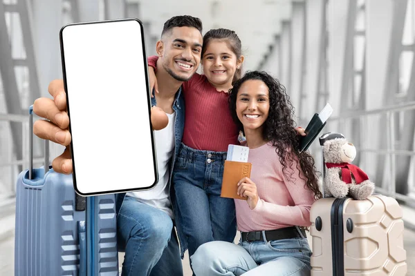 Fajna aplikacja. Happy Arab Family Pokazuje pusty smartfon podczas oczekiwania na lotnisku — Zdjęcie stockowe