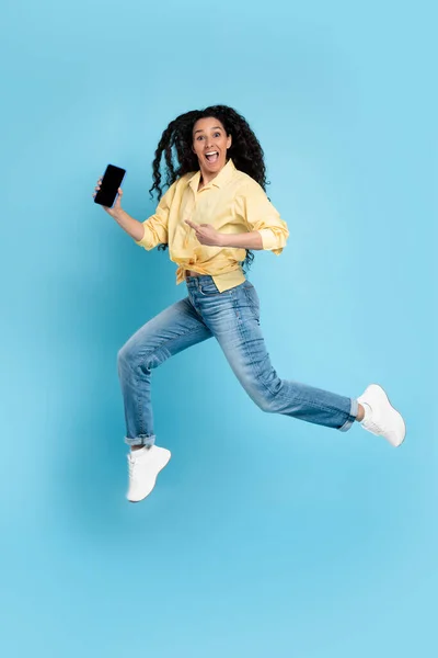 Cheerful lady jumping and pointing at empty smart phone screen — Foto de Stock