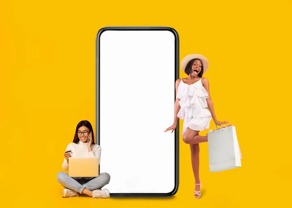 Women posing with white empty smartphone screen and shopper bags — Stockfoto