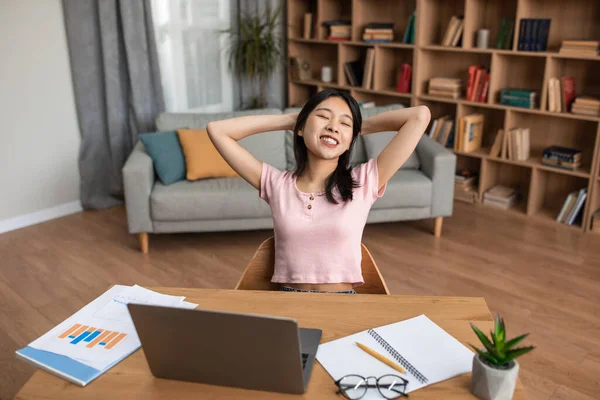 Relaxado jovem asiático senhora sentado com as mãos atrás cabeça perto laptop, tendo quebrar depois on-line classe ou trabalho em casa — Fotografia de Stock