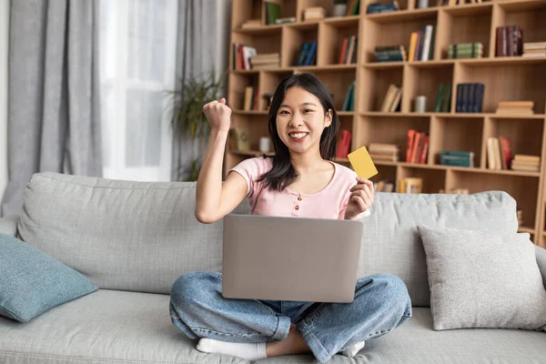 Overjoyed korean woman with laptop computer and credit card making YES gesture over big discount, sitting at home — Foto Stock