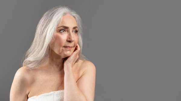 Kecses öregedési koncepció. Vonzó idős hölgy megható bőr az arcán át szürke stúdió háttér, panoráma — Stock Fotó