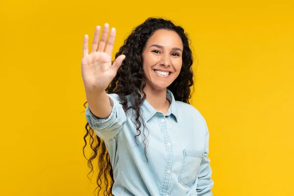 Portrait of happy young woman showing palm at yellow studio — Foto de Stock