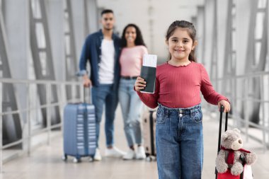 Çantası ve pasaportu olan küçük bir Arap kız havaalanında ailesiyle poz veriyor.