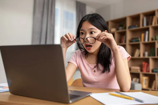 Inacreditável. Chocado asiático senhora no óculos olhando para laptop tela do computador, sentado na mesa em casa — Fotografia de Stock