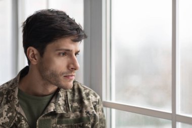 Evinin penceresinden bakan mutsuz bir asker.