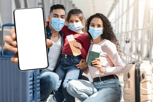 Arab Family Wearing Medical Masks Demonstrating Smartphone With Blank Screen At Airport —  Fotos de Stock