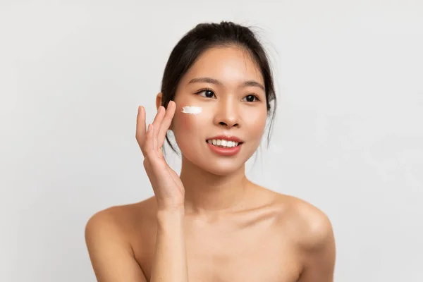 Portrait of Asian woman touching applying cream on cheeks — Stockfoto