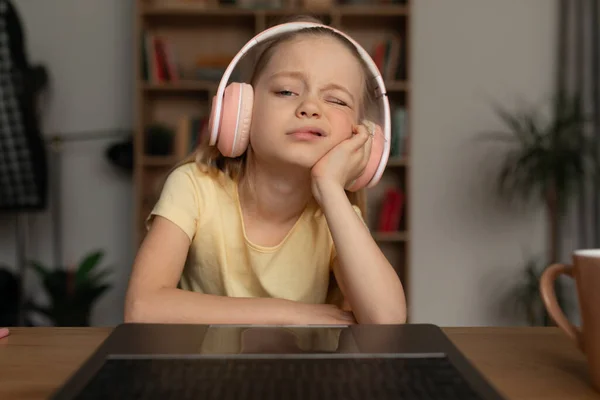 Uttråkad liten flicka med bärbar dator bär hörlurar hemma — Stockfoto