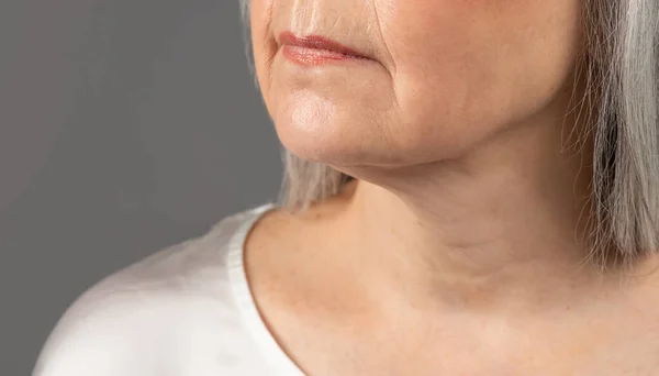 Mature skin care. Cropped view of senior womans face with wrinkles around lips and on neck, grey studio background — Foto Stock