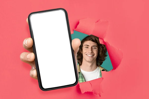 Cheerful guy showing white empty smartphone screen through torn paper — 스톡 사진