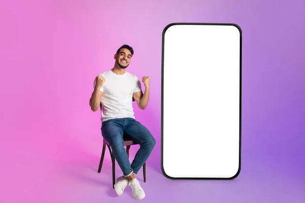 Young Arab guy offering huge smartphone with mockup, gesturing YES, advertising web store, casino or lottery app — ストック写真