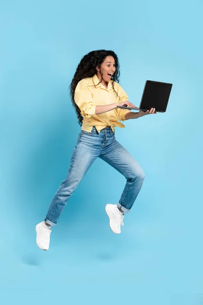 Excited woman using laptop jumping up in air at studio
