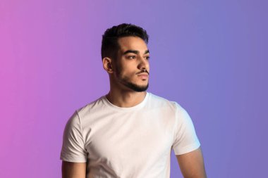 Beyaz tişörtlü, parlak ışıkta poz veren ve başka yöne bakan ciddi bir Arap.