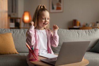Schoolgirl Using Laptop Shaking Fists Celebrating Educational Success At Home