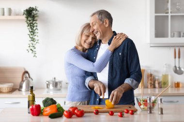 Mutlu son sınıf kadını kocasına sarılıyor, yemek pişiriyor.