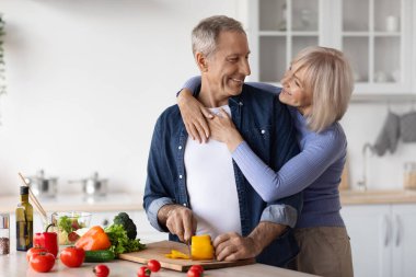 Loving senior couple making healthy salad together in kitchen