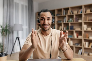 Kulaklık takan, internetten video görüşmesi yapan, iş ortağıyla konuşan ve kameraya el kol hareketi yapan pozitif Arap serbest çalışan bir adam.