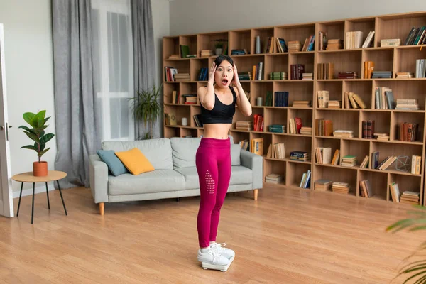 Shocked asian lady grabbing her head in terror, standing on scales, failing to achieve weight loss goal, free space — Stockfoto