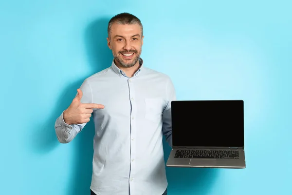 Homem de meia idade segurando laptop apontando o dedo sobre fundo azul — Fotografia de Stock