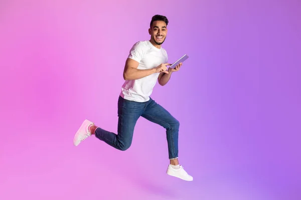 Akıllı telefonlu mutlu genç Arap adam neon ışıkta zıplıyor, uzayı kopyalıyor. Havalı yeni uygulama, web sitesi veya reklam — Stok fotoğraf